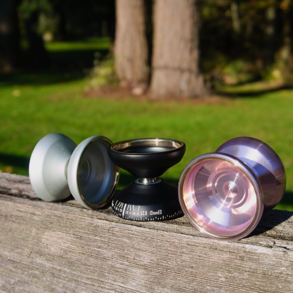 Silver, black, and rose colored Exia yoyos on a wood surface, outdoors.
