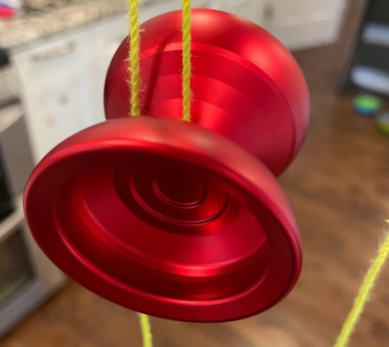 Close up wide angle shot of a red yoyo prototype spinning, attached to a yellow yoyo string. A kitchen is out of focus in the background.